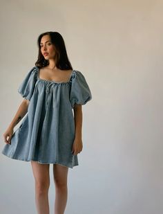 a woman standing in front of a white wall wearing a denim dress with puffy sleeves