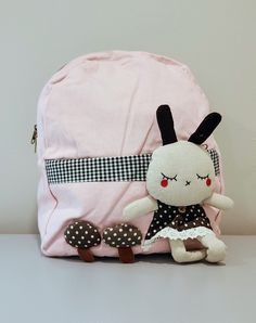 a pink backpack with a stuffed bunny sitting next to it