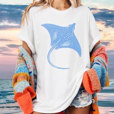 Celebrate the beauty of the ocean with our artisan-printed stingray shirt. Each design captures the grace and mystery of these gentle sea creatures, known for their fluid movement and unique elegance. Perfect for ocean lovers and anyone who appreciates marine life. SIZING: Unisex Adult Sizing ensures a comfortable fit for all (If you prefer a loose fit go one size up. For the trendy oversized tee, consider 1-2 sizes up.) If you are unsure, simply measure your favorite tshirt on a flat surface an Cotton T-shirt With Shark Design For Summer, Casual Short Sleeve Shark Design Tops, Summer Short Sleeve T-shirt With Shark Design, Casual Short Sleeve Top With Shark Design, White Crew Neck Top With Shark Design, Casual Summer T-shirt With Shark Design, Casual White Shark Design Tops, White Casual Tops With Shark Design, Casual White Tops With Shark Design