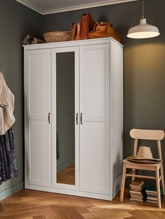 a white armoire sitting in a room next to a wooden chair and a lamp