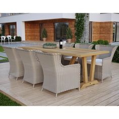 an outdoor dining table and chairs on a wooden deck in front of a modern house