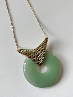 This unique pendant features a green aventurine donut, a semi-precious stone valued for its natural beauty and energetic properties. The bail, delicately woven with pearls, brings a touch of sophistication and craftsmanship to this jewel. The elegant design and quality materials make this pendant an exceptional piece to add to your jewelry collection. Natural Stone: Green aventurine is renowned for its calming properties and its ability to attract luck and prosperity. Attract Luck, Donut Pendant, Unique Pendant, Green Aventurine, Semiprecious Stones, Natural Stone, Semi Precious, Natural Stones, Elegant Design