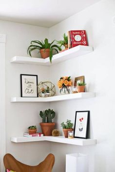 some white shelves with plants and pictures on them in the corner of a living room