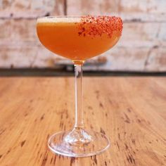 an orange drink with sprinkles in a wine glass on a wooden table