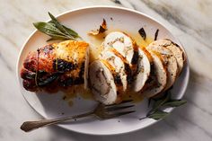 a white plate topped with sliced chicken and sauce on top of a marble countertop