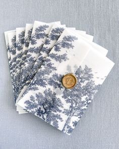 six blue and white napkins with trees printed on the front, one has a gold button