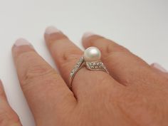 a person's hand with a pearl and diamond ring on top of their finger