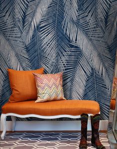 an orange bench sitting in front of a blue and white wall with palm leaves on it