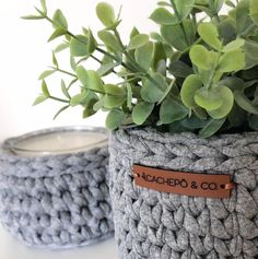 two gray crocheted baskets sitting on top of a table next to a potted plant