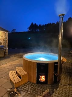 a hot tub sitting on top of a stone patio next to a fire place and bench