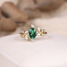 an emerald colored ring with white diamonds on the bottom and gold band, sitting on top of a pillow