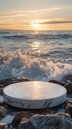 a white frisbee sitting on top of some rocks near the ocean at sunset