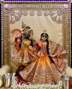 two figurines sitting next to each other in front of a wall with flowers