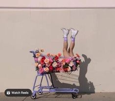 a woman laying on top of a shopping cart with flowers in the front and legs