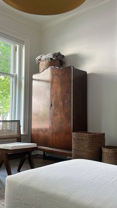 a bedroom with a bed, dresser and basket on the floor in front of a window