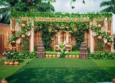 an outdoor wedding setup with greenery and gold vases on the grass in front of it