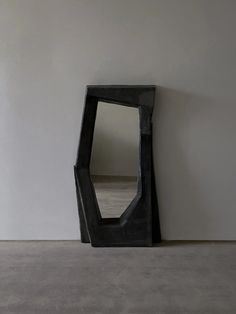 a black mirror sitting on top of a cement floor next to a white wall in an empty room