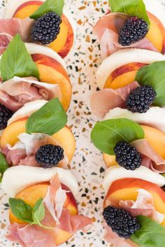 an assortment of fruits and meats are arranged on a platter with basil leaves