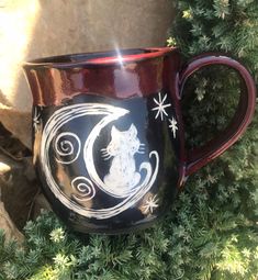 a black and white cat sitting on top of a red coffee cup with the moon painted on it