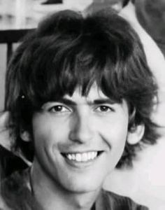 a black and white photo of a man with long hair smiling in front of a wall