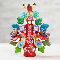 a red vase filled with lots of colorful flowers and birds sitting on top of it