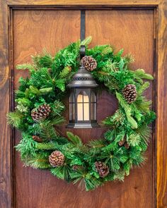 a green wreath with pine cones hanging on a wooden door handle and lantern light attached to it