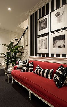 a red couch with black and white pillows is in front of some pictures on the wall