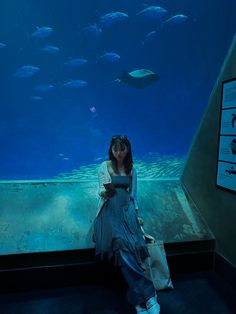 a woman sitting in front of an aquarium looking at her cell phone