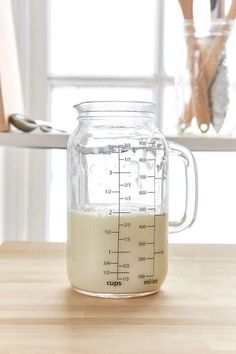 a glass jar filled with liquid sitting on top of a wooden table next to utensils