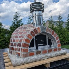 an outdoor brick pizza oven sitting on top of a wooden pallet with trees in the background