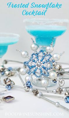 two cocktail glasses filled with blue liquid and silver beaded snowflakes on the rim