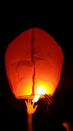 a person holding up a red paper lantern in the dark with light coming from it