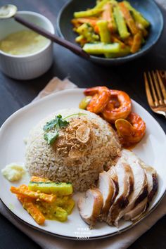 a white plate topped with rice covered in meat and veggies next to a bowl of sauce