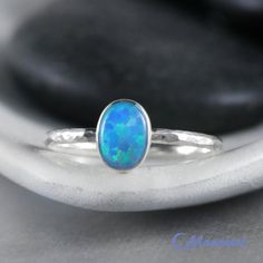 This Sterling Silver Blue Opal Ring features an 8 mm x 6 mm oval lab grown Blue Opal cabochon that has been securely set in a highly polished fine silver bezel. The band is made of a sturdy round Sterling Silver wire that has a hammered texture around the entire band. These beautiful rings make unique promise rings, lovely stacking rings, great birthstone rings, or just a wonderful love tokens for yourself or your special someone.This man-made Blue Opal is created from very uniform nanoparticles Classic Blue Oval Opal Ring, Classic Blue Opal Ring As A Gift, Classic Blue Opal Ring As Gift, Classic Blue Opal Ring For Gift, Classic Blue Opal Ring Gift, Classic Blue Opal Round Ring, Stackable Oval Opal Rings, Classic Blue Oval Cabochon Rings, Blue Cabochon Opal Ring For Anniversary