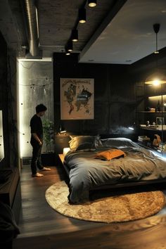 a man standing next to a bed in a room with dark walls and wooden floors