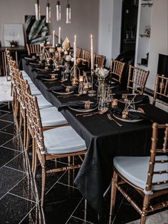 a long table is set with black and white linens, gold candlesticks, and silver plates