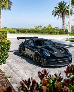 a black sports car parked in front of palm trees on a brick driveway next to some bushes