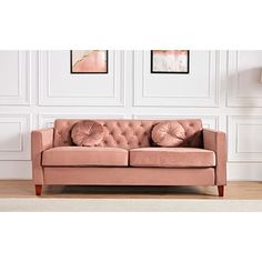 a pink couch sitting on top of a wooden floor next to a lamp and paintings