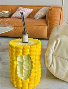 a yellow corn cob table with a bottle on top and a couch in the background