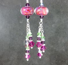 Handmade glass dangle earrings featuring pink, purple and green SRA artisan crafted boro lampwork beads; sterling silver; and Fuchsia, Amethyst AB and Peridot AB  crystals. These beautiful earrings are composed of 14mm artisan crafted borosilicate glass beads. The beads have swirls of pink, purple and green encased within crystal clear glass. Fuchsia, Amethyst AB and Peridot AB  crystals dangle below and add sparkle.  Sterling silver beads and headpins complete these earrings,  The  earrings are suspended from sterling silver ear wires. These earrings are 3 inches (7.6 cm) long measured from the top arch of the sterling silver ear wire. More Boro Lampwork Glass Earrings http://www.etsy.com/shop/GlassRiverJewelry?section_id=6993958 Thank you for visiting GlassRiverJewelry.etsy.com Purple Czech Glass Dangle Earrings, Purple Dangle Earrings With Czech Glass, Purple Czech Glass Earrings With Dangling Beads, Pink Czech Glass Dangle Earrings, Purple Czech Glass Drop Earrings, Pink Czech Glass Drop Earrings, Purple Czech Glass Earrings For Gift, Pink Czech Glass Pierced Earrings, Purple Glass Dangle Earrings