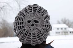 a woman wearing a crocheted skull hat in front of a snow covered field