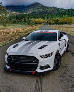 a white mustang car parked on the side of the road with mountains in the background