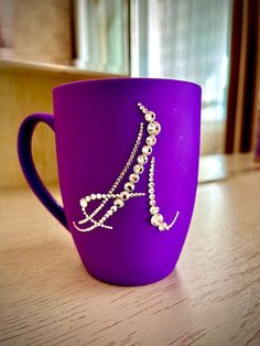 a purple coffee cup with pearls on the side and a chain hanging from it's handle