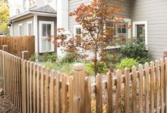 a wooden fence in front of a house with a tree and bushes behind the fence