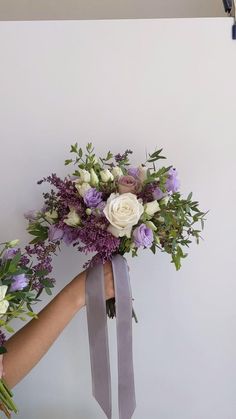 a bouquet of flowers being held by someone's hand on a white wall background