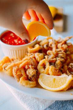 a person is dipping sauce on some fried food with lemon wedges and ketchup