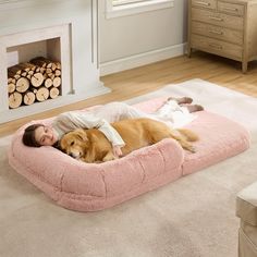 a woman laying on top of a dog bed next to a fire place