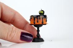 a hand holding a miniature cake with orange and black icing on it's top