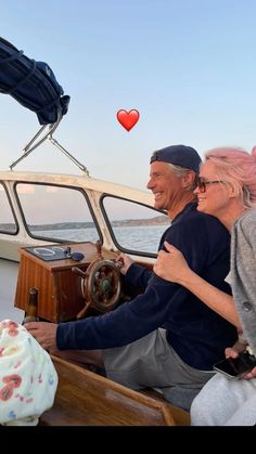 an older couple sitting on a boat in the ocean with a heart shaped balloon floating above them