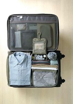 an open suitcase filled with clothes on top of a wooden floor next to a wall